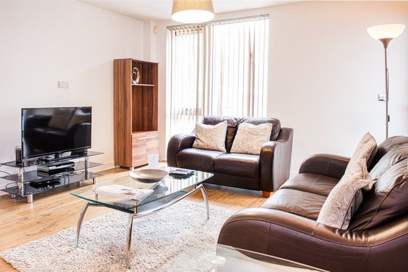 Spacious living room with brown leather sofas, glass coffee table, TV, wooden storage unit and large windows