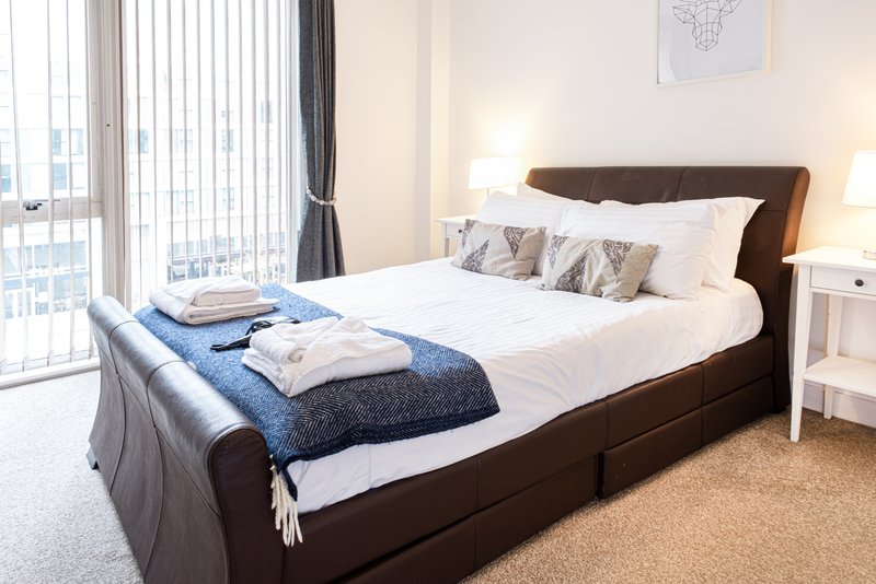 Modern bedroom with dark brown bed, white bedding, blue throw, and floor-to-ceiling windows