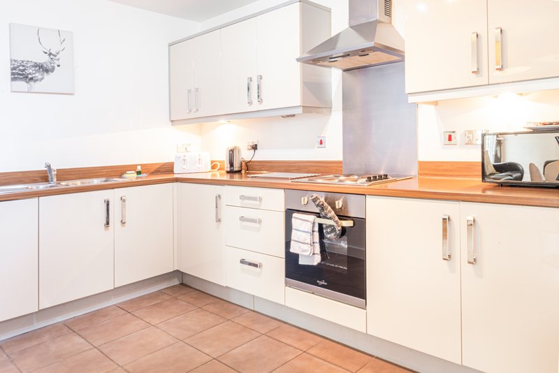 Modern kitchen with white cabinetry, wooden worktops, stainless steel appliances and tiled floor