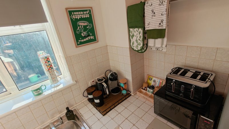 Small kitchen with cream tiles, window, black toaster, kettle, and wall-mounted organizers