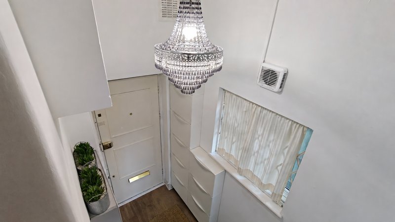 Hallway with white door, crystal chandelier, chest of drawers and window blind