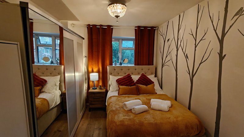 Bedroom with double bed, gold bedspread, burgundy pillows, mirrored wardrobe and tree wall decals