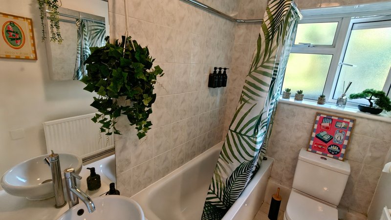 Bathroom with sink, toilet, bathtub, hanging plants, and window with natural light