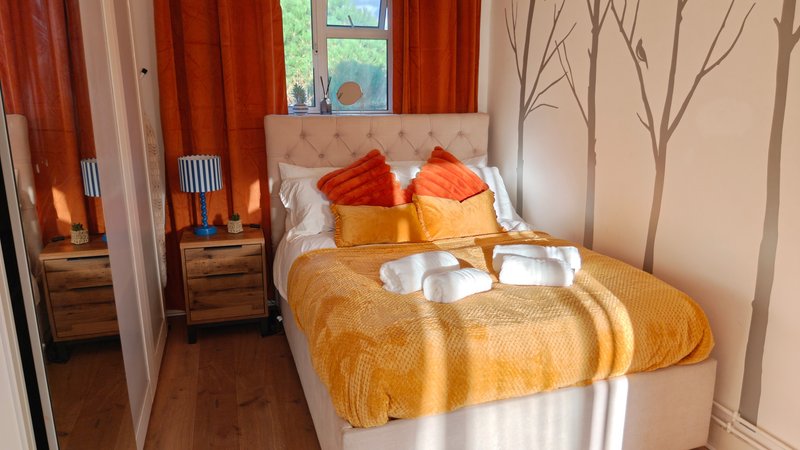 Bedroom with double bed, orange bedding, red cushions, wooden nightstands and warm lighting