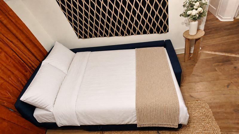Bedroom with double bed, white bedding, navy frame, wooden floor and decorative cushion