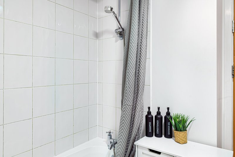 Modern bathroom with white subway tiles, shower head, grey curtain, and shelf with bottles and plant