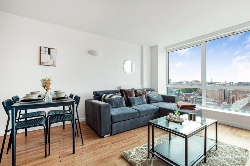 Modern open-plan living room with dining table, sofa, and large windows overlooking cityscape