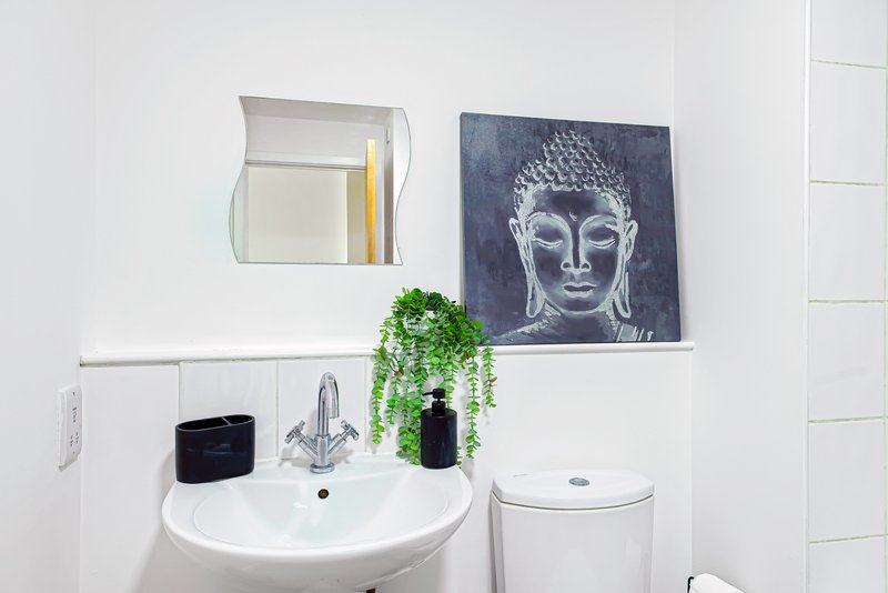 Modern bathroom with white sink, mirror, Buddha artwork, and hanging green plant