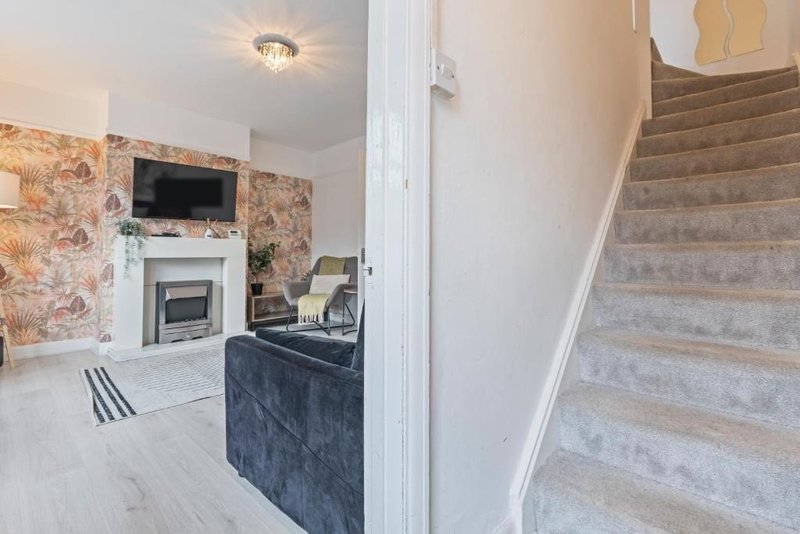 Open-plan living area with fireplace, TV, dark kitchen island and wooden staircase