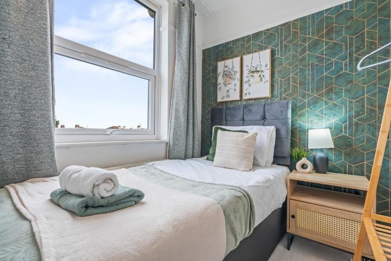 Modern bedroom with double bed, green geometric wallpaper, wooden nightstand and window view