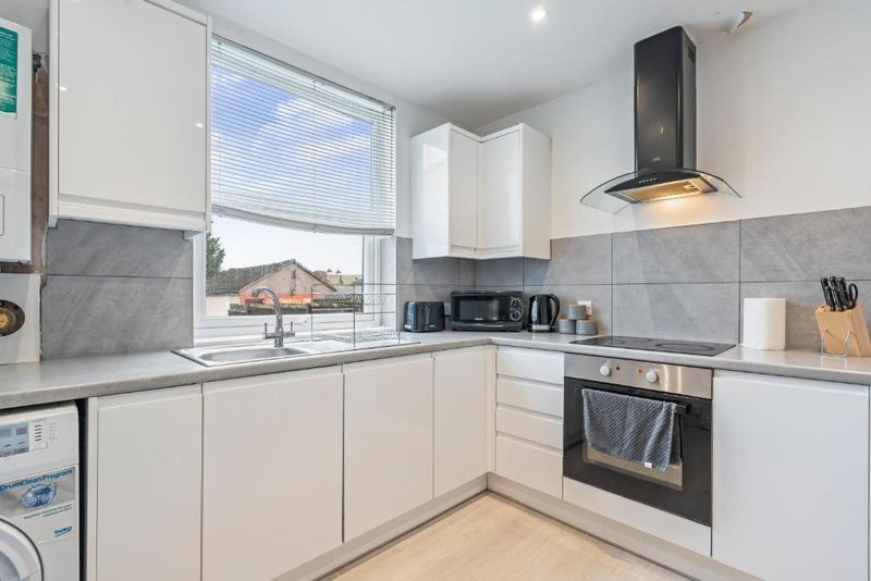 Modern kitchen with white cabinetry, gray tile splashback, black appliances and window view