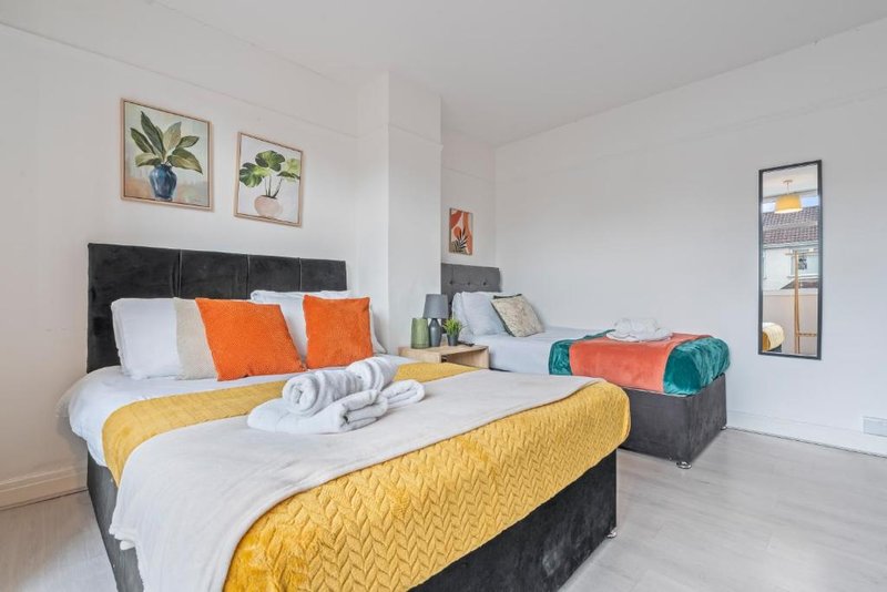 Bright bedroom with double bed, yellow bedding, orange pillows, and potted plants on walls