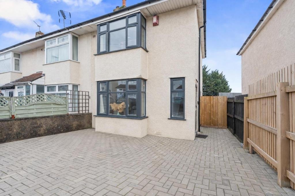 Semi-detached house exterior with paved driveway, wooden fence, and manicured garden