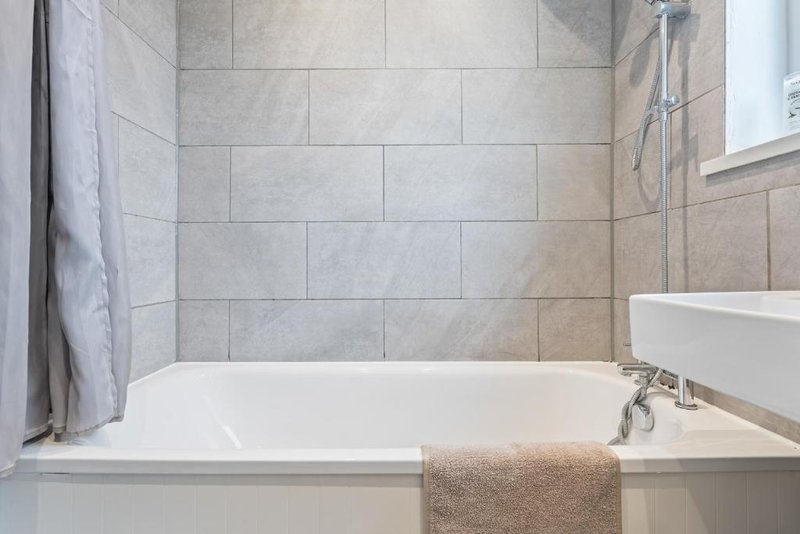 Modern bathroom with white bathtub, gray tile walls, and beige towel