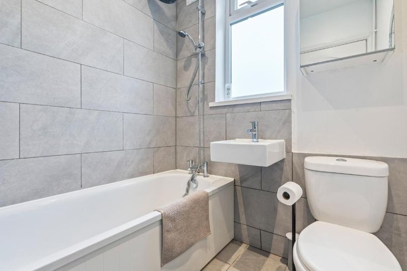 Modern bathroom with white bathtub, wall-mounted sink, toilet, and tiled walls