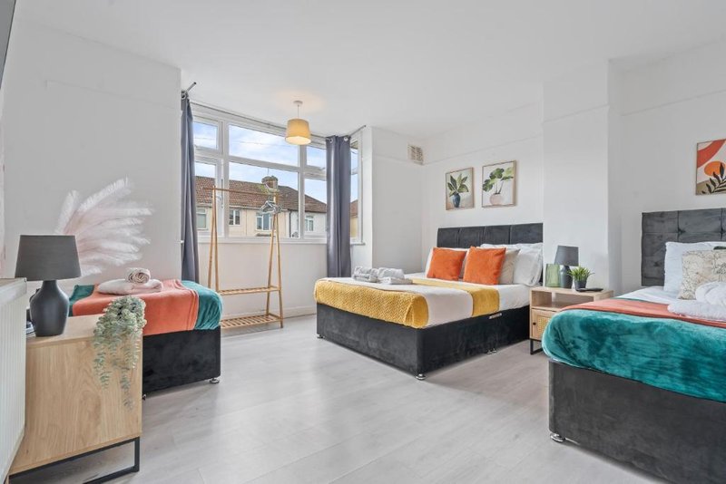 Bright bedroom with multiple beds, colorful pillows, plants, and large windows