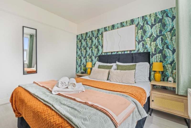 Bright bedroom with double bed, orange throw, patterned green headboard wallpaper and bedside lamps