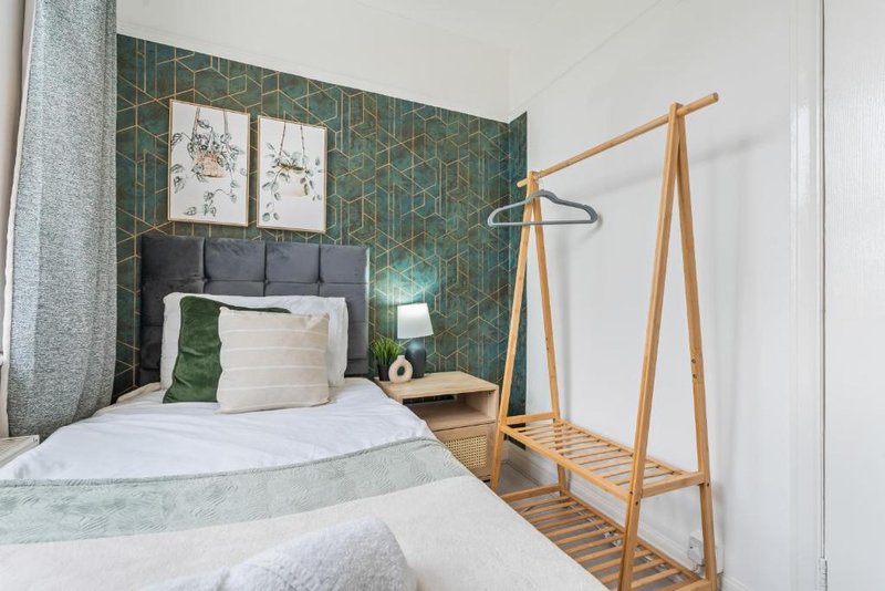 Bedroom with single bed, green geometric wallpaper, wooden clothing rack and framed botanical prints