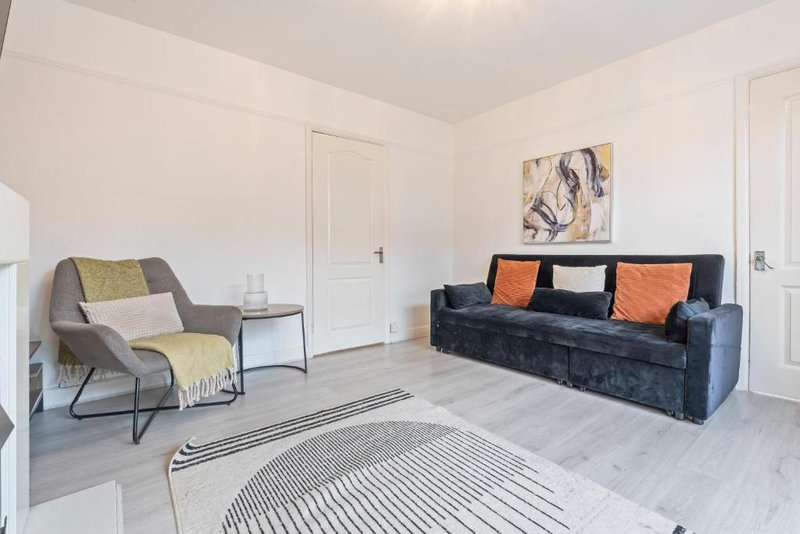 Bright living room with gray armchair, dark sofa with orange cushions, and striped rug