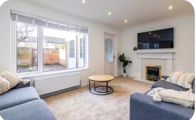 Bright living room with blue sofas, fireplace, wall-mounted TV, and large windows overlooking garden