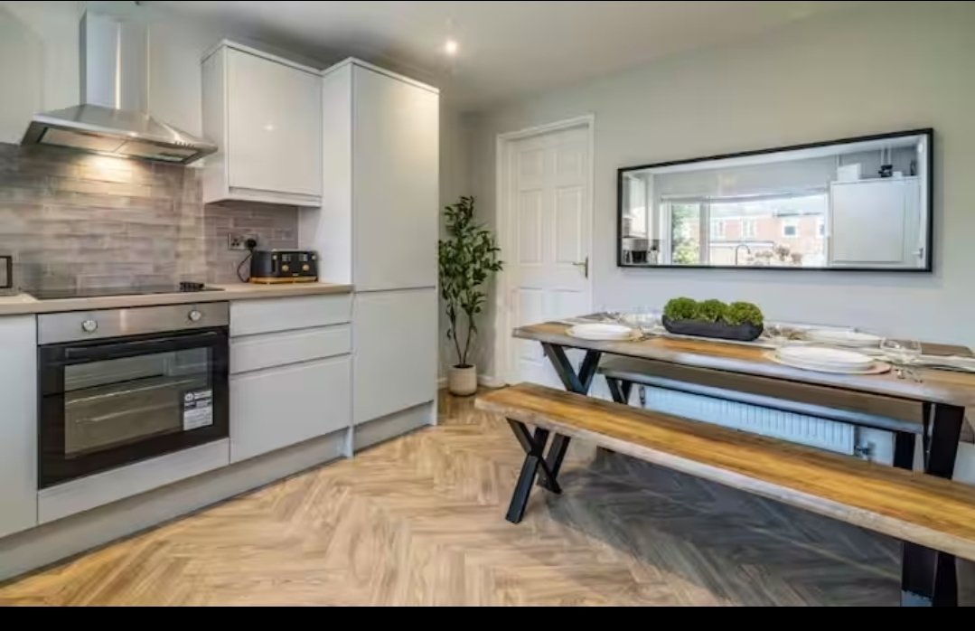 Modern open-plan kitchen and dining area with white cabinetry, wooden table, and wall-mounted TV