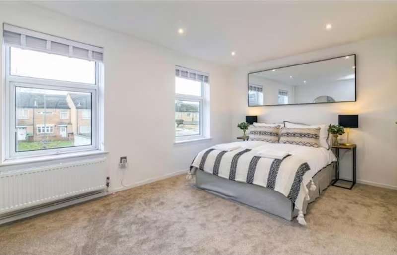 Bright bedroom with double bed, striped bedding, large mirror, and two windows overlooking street