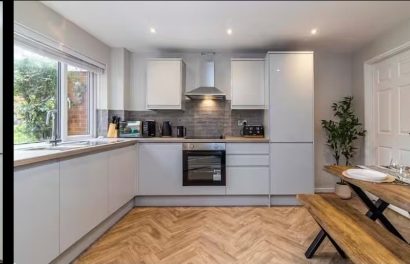 Modern white kitchen with herringbone wood flooring, built-in appliances, and dining table