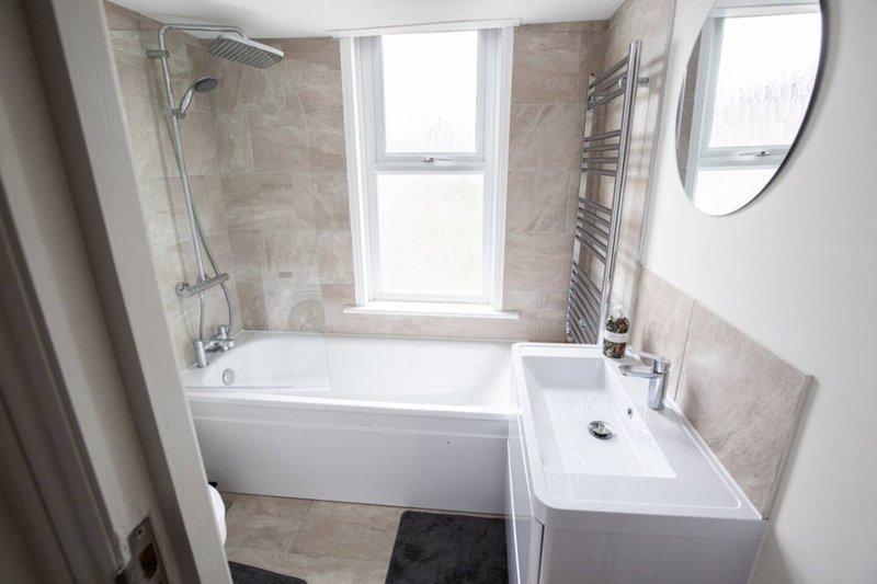 Modern bathroom with white bathtub, sink, tiled walls, window and heated towel rail