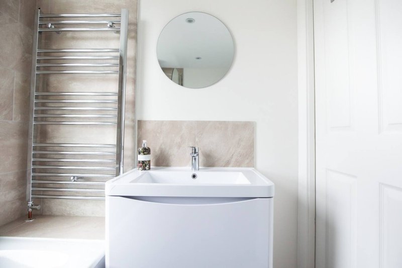 Modern bathroom with white vanity sink, circular mirror, chrome towel rail and tiled walls