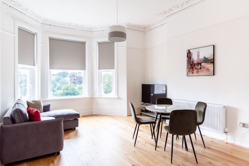 Bright open-plan living room with sofa, dining table, chairs, and bay windows