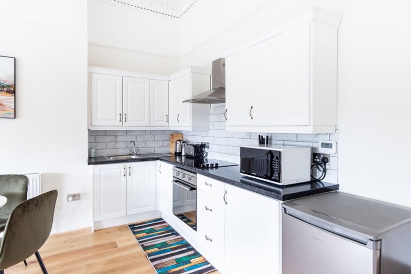 Modern white kitchen with stainless steel appliances, tiled backsplash, and wooden flooring