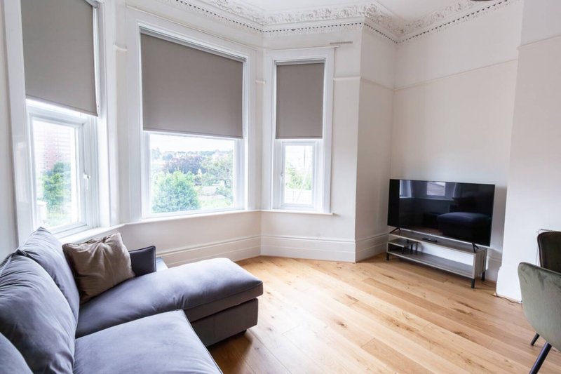 Bright living room with blue sofa, wooden floor, bay windows and wall-mounted TV