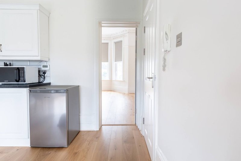 Bright kitchen with white cabinetry, stainless steel appliances, wooden flooring and open doorway