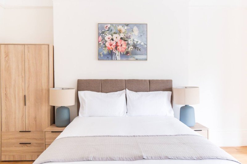 Modern bedroom with double bed, brown upholstered headboard, white bedding, wooden wardrobe and floral wall art