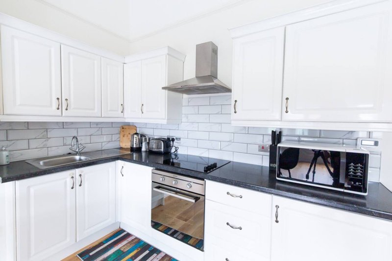 Modern white kitchen with dark countertops, stainless steel appliances, and subway tile backsplash