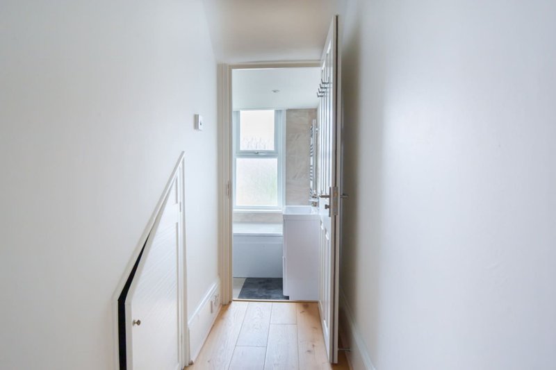 Narrow hallway with white walls, wooden flooring, and open doorway to kitchen area