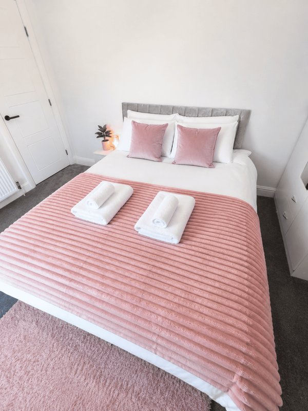 Bedroom with double bed, pink bedding, grey headboard, white pillows and potted plant