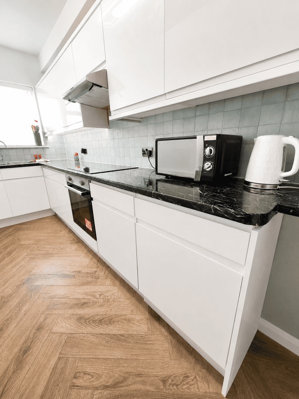 Modern kitchen with white cabinetry, black granite countertop, stainless steel appliances and wooden flooring