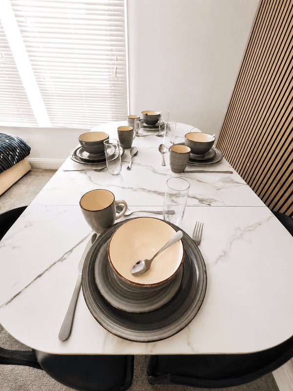 Dining table set for three with marble top, place settings and tableware by windows
