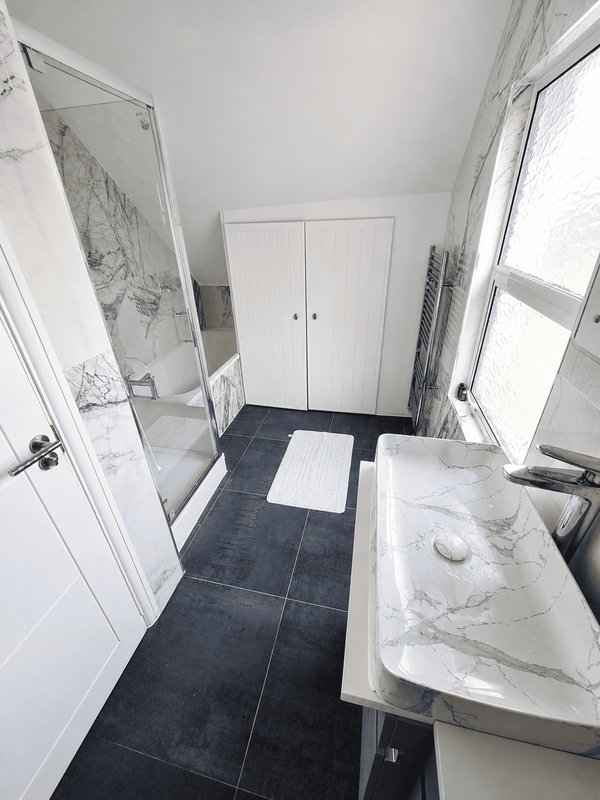 Clean bathroom with dark tile floor, white sink vanity, shower enclosure and white wardrobe