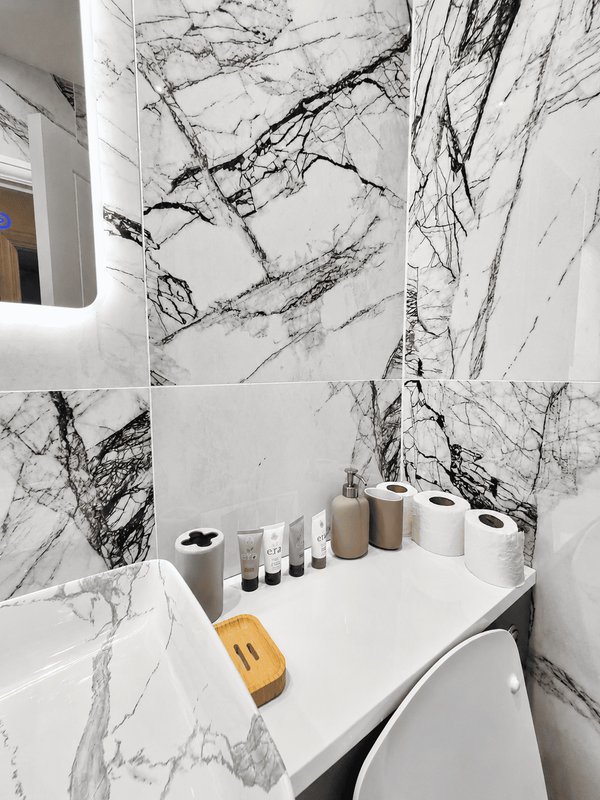 Modern bathroom with marble-effect tiling, white sink, toiletries and bathroom products on counter