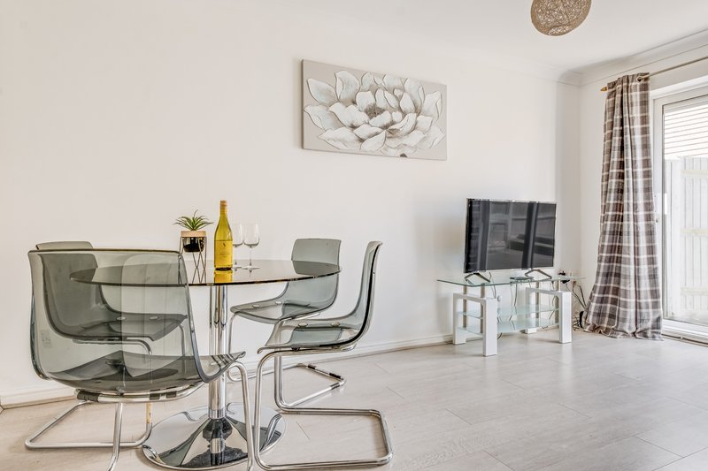 Open-plan living area with glass dining table, modern chairs, TV unit and wall art