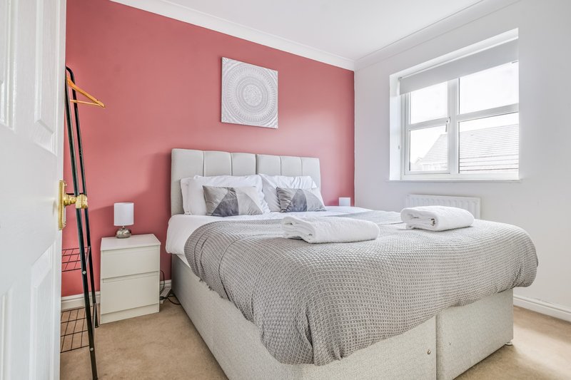 Bright bedroom with pink walls, double bed, white bedding, wooden floor and large window