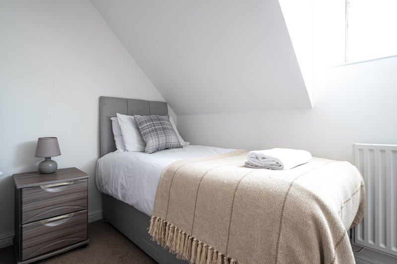 Bright attic bedroom with single bed, grey headboard, bedside table and lamp