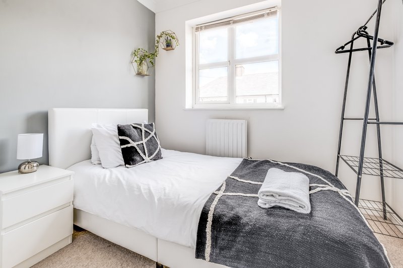 Bright modern bedroom with white bed, grey and black bedding, pendant lamp and coat stand