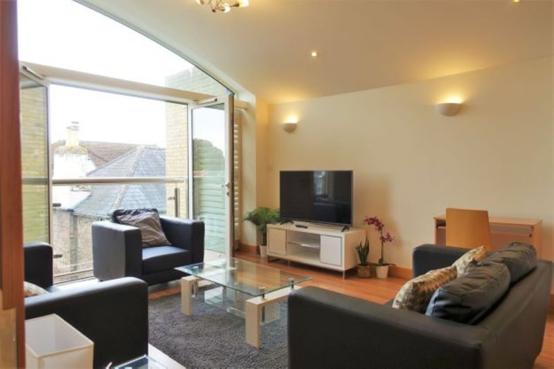 Modern living room with black sofas, TV, large windows, wooden flooring and warm lighting