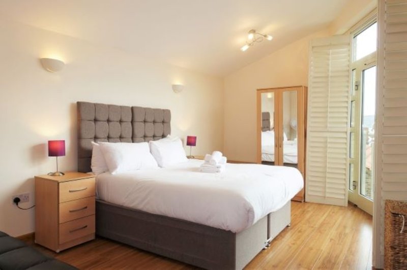 Bright bedroom with double bed, tufted headboard, wooden nightstands, and glass patio doors