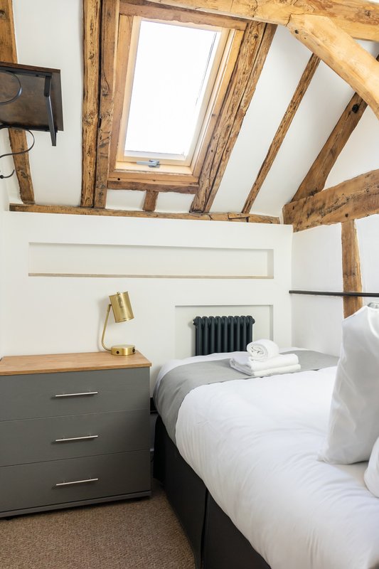 Bedroom with exposed wooden beams, skylight, single bed, dark dresser and brass lamp