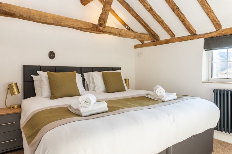 Bedroom with exposed wooden beams, double bed, olive cushions, rolled towels and window