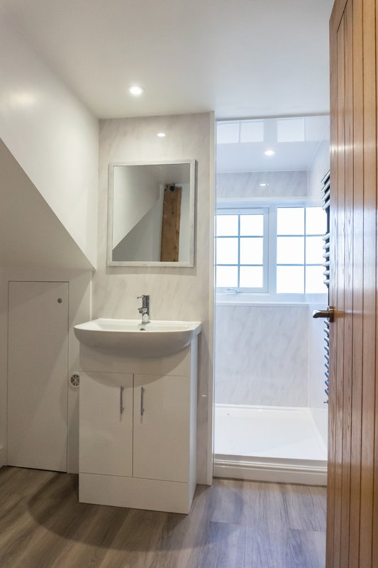 Modern bathroom with white vanity sink, mirror, and wooden door leading to shower area